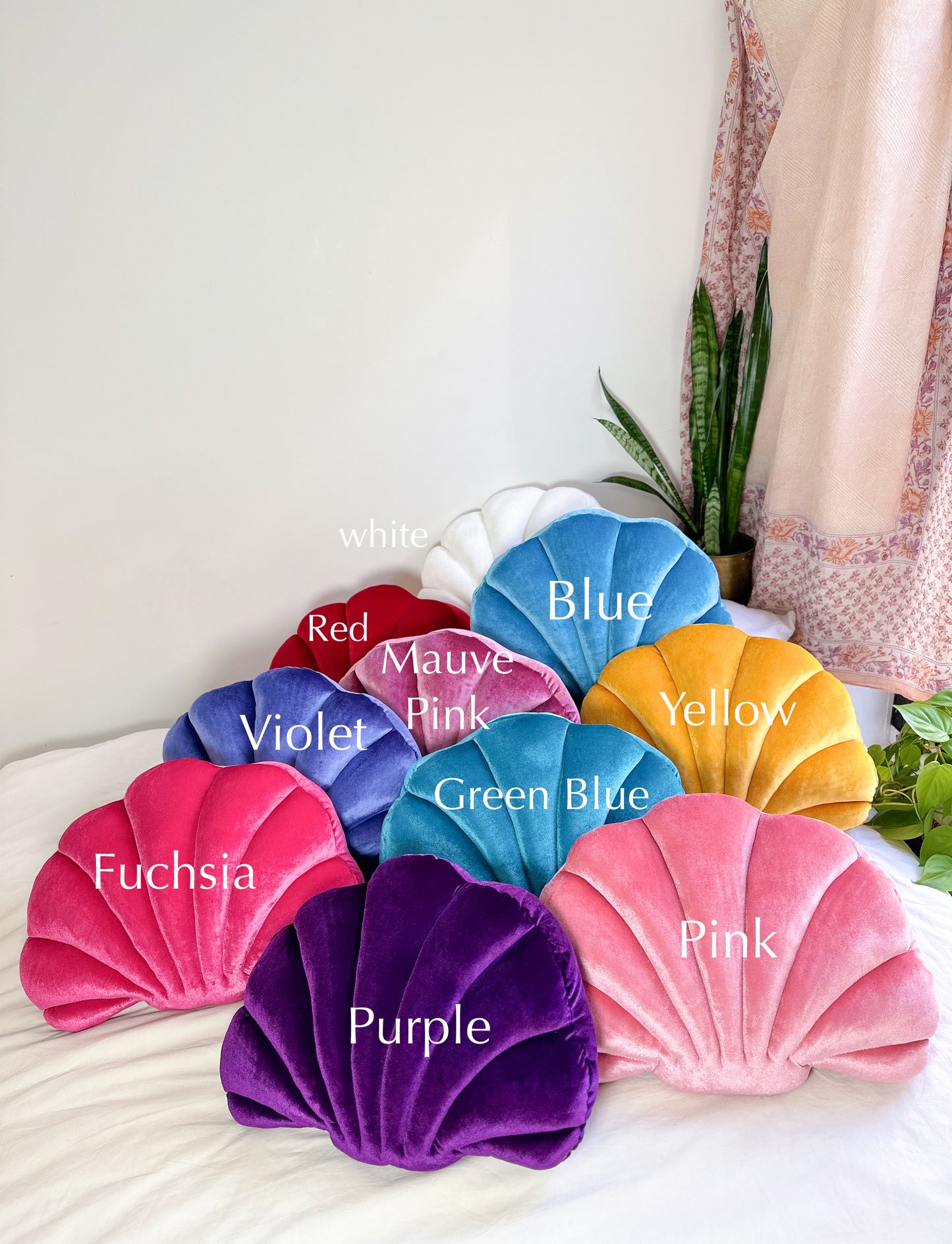 Shell pillows on a bed with the corresponding color listed on each pillow