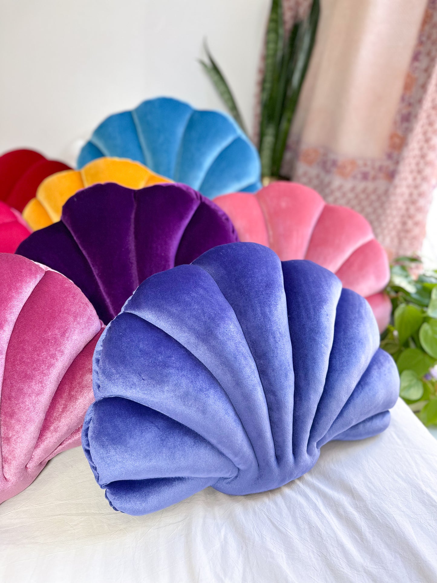 colorful shell shaped pillows on a bed with a violet shell pillow in the front