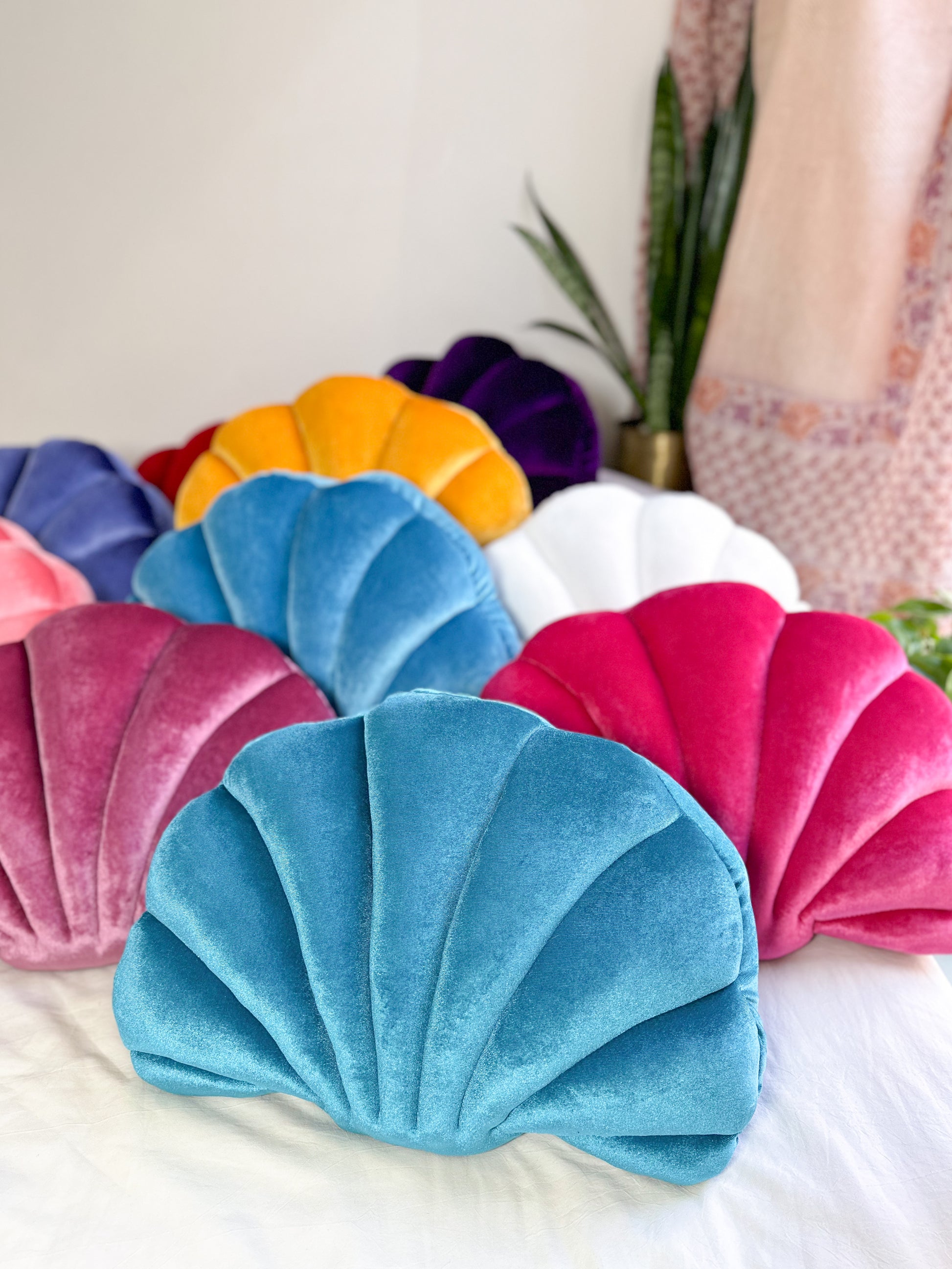 colorful shell shaped pillows on a bed with a green blue shell pillow at the front